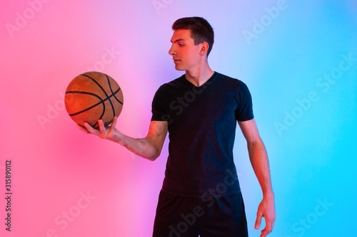 Young athletic man, with basketball, posing on background with neon lights © Shopping King Louie