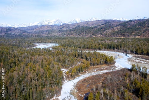 frozen river in the forest against the backdrop of snowy mountains