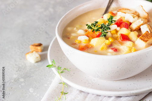 Bowl of homemade corn chowder soup with potatoes, carrots, red bell pepper and croutons on a light grey stone background. Delicious cozy first course, comfort food. photo
