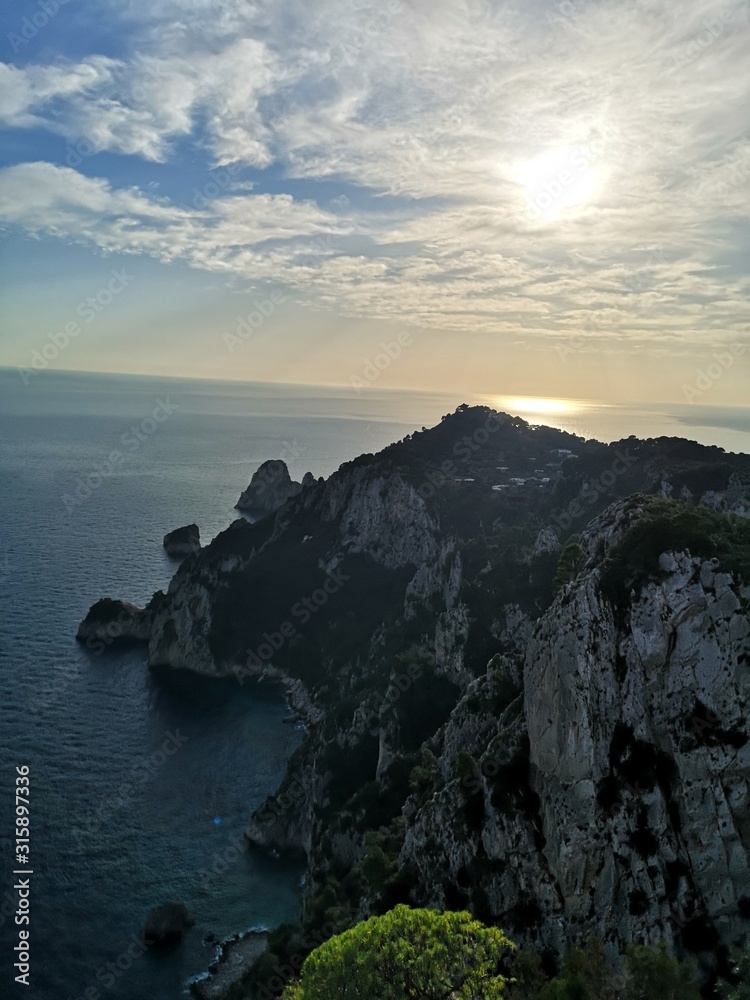 Coastal cliffs hanging over the sea on Capri island with the sunset in the background