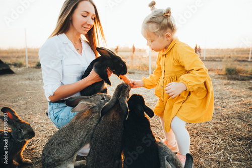 Mom and daughter visit a petting zoo with rabbits on the eve of Easter. Holiday, Easter traditions.