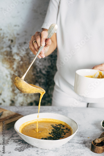 A woman serving pumpkin soup in a bowl