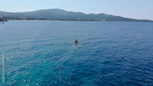 Drone aerial shot of small wooden fishing boat in crystal clear blue waters of Greece coastline.