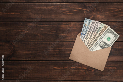 Close-up kraft paper envelope with one hundred dollar bills on brown wooden background, bundle of money is a concept of corruption, bribe and the black economy, top view, copy space photo