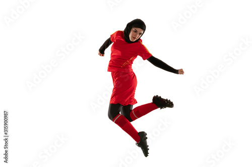 Arabian female soccer or football player isolated on white studio background. Young woman kicking the ball back, training, practicing in motion and action. Concept of sport, hobby, healthy lifestyle.