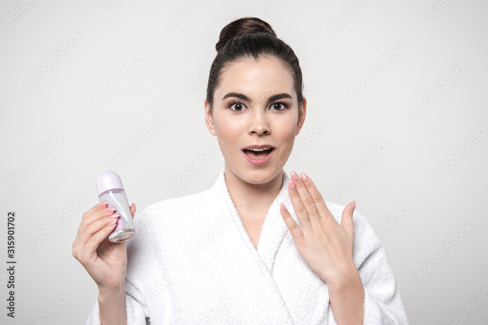 shocked woman in bathrobe holding deodorant while looking at camera isolated on grey shocked woman in bathrobe holding deodorant while looking at camera isolated on grey