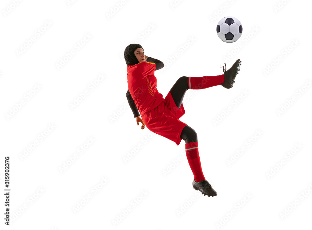 Arabian female soccer or football player isolated on white studio background. Young woman kicking ball in jump, catched in air, training in motion, action. Concept of sport, hobby, healthy lifestyle.