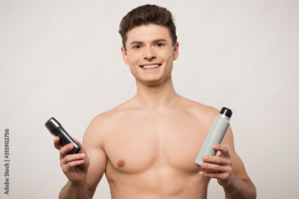 smiling shirtless man looking at camera while holding deodorants isolated on grey smiling shirtless man looking at camera while holding deodorants isolated on grey