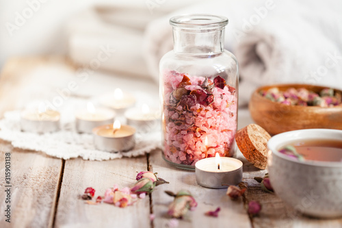 Concept of spa treatment with roses. Crystals of sea pink salt in bottle, candles as decor. Atmosphere of relax and pleasure. Anti-stress and detox procedure. Luxury lifestyle. Wooden background