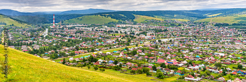 Panoramic view from hill to plain with small town in summer cloudy day. Picturesque urban landscape with many colorful houses. Sim, Chelyabinsk region, Russia. Travel blog concept
