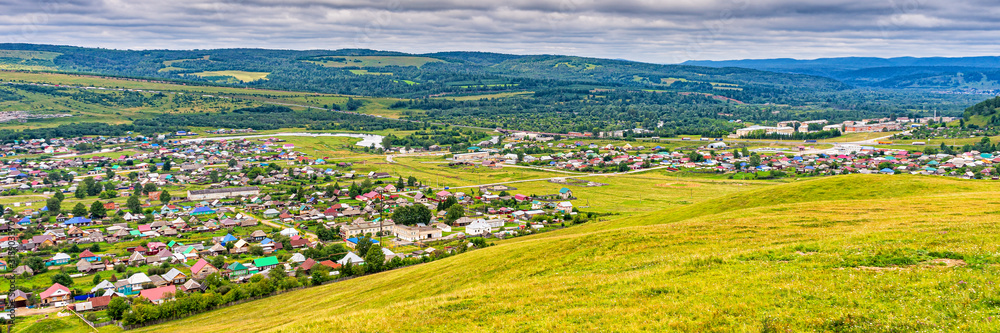 Panoramic view from hill to plain with small town in summer cloudy day. Picturesque urban landscape with many colorful houses. Sim, Chelyabinsk region, Russia. Travel blog concept