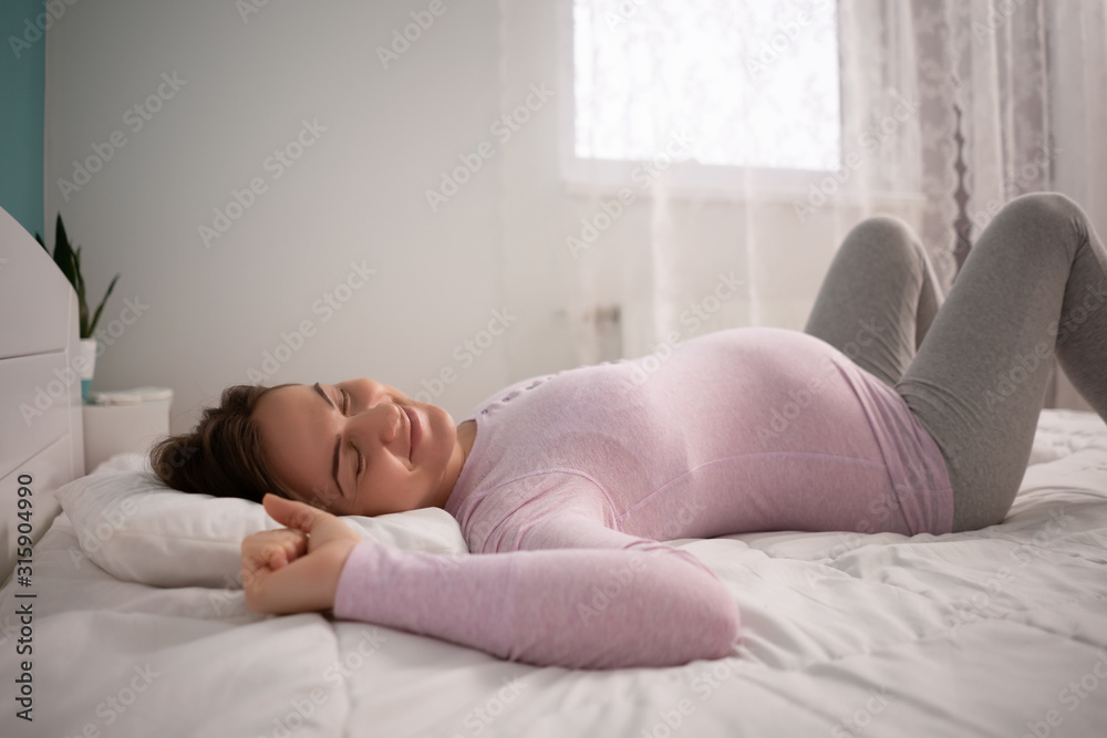 Pregnant woman is sleeping and stretching in her bed. Pregnant woman is sleeping and stretching in her bed.