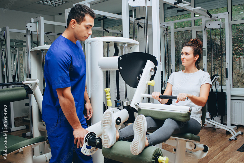 Rehabilitation specialist shows the patient how correctly doing exercise on the exercise machine to restore muscle