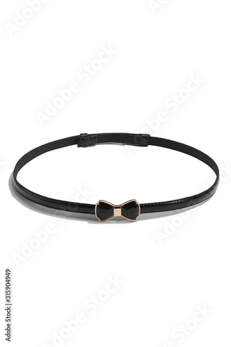 Subject shot of a thin belt made of black patent leather and decorated with a figured buckle in the form of a black bow-knot in golden setting. The stylish belt is isolated on the white background.