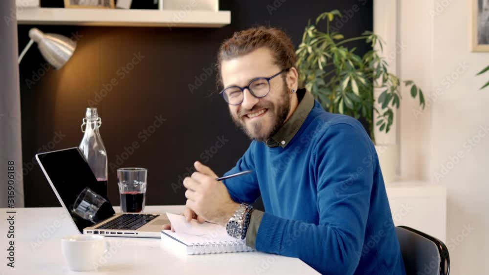 Inovative young caucasian freelancer sitting in his office, using laptop for internet search and writing in notebook results of searching. Inovative young caucasian freelancer sitting in his office, using laptop for internet search and writing in notebook results of searching.
