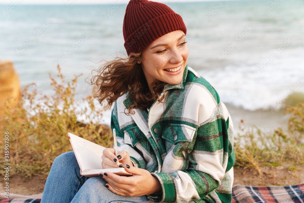 Image of happy woman smiling and making notes in diary while sitting