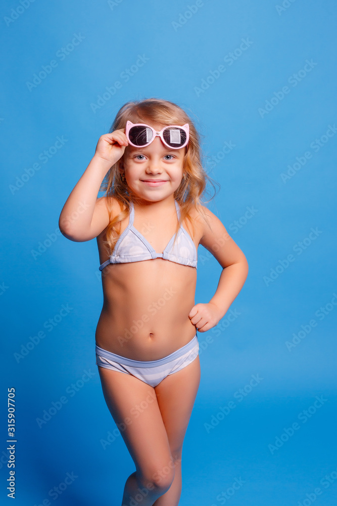 little blonde girl in sunglasses and swimsuit on a blue background little blonde girl in sunglasses and swimsuit on a blue background