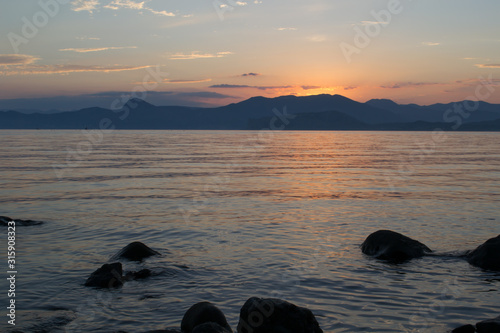  Yellow beautiful sunset. The sun sets over the mountains  in the foreground is a sea or a lake and stones. Great view. Photo in the dark.