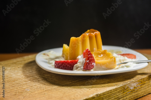 postre flan de vainilla con fresas y nata en plato blanco photo