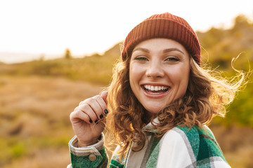 Image of young woman wearing hat and plaid shirt walking outdoors
