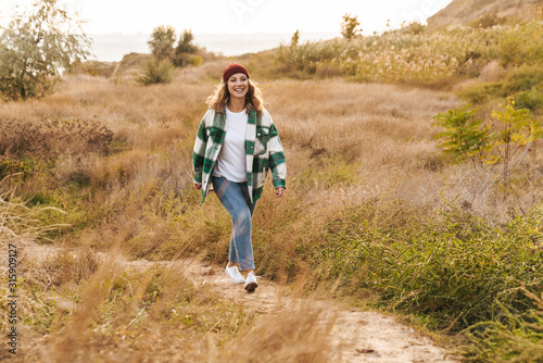 Image of young woman wearing hat and plaid shirt walking outdoors