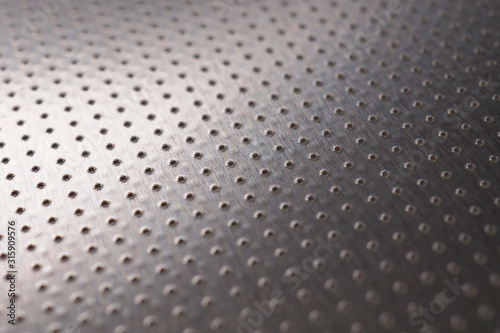 Aluminum surface with many holes. Their ranks go into the distance and form a perspective. Abstract dark gray metal background or wallpaper. Macro