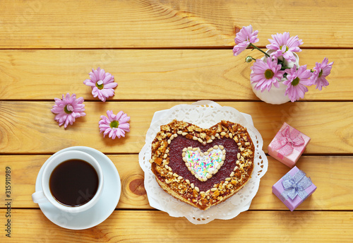 A beautiful congratulation on Valentine s Day or Happy Birthday  fresh homemade heart-shaped cake and a bouquet of flowers on wooden table. Festive background  flat lay  copy space  top view  close-up