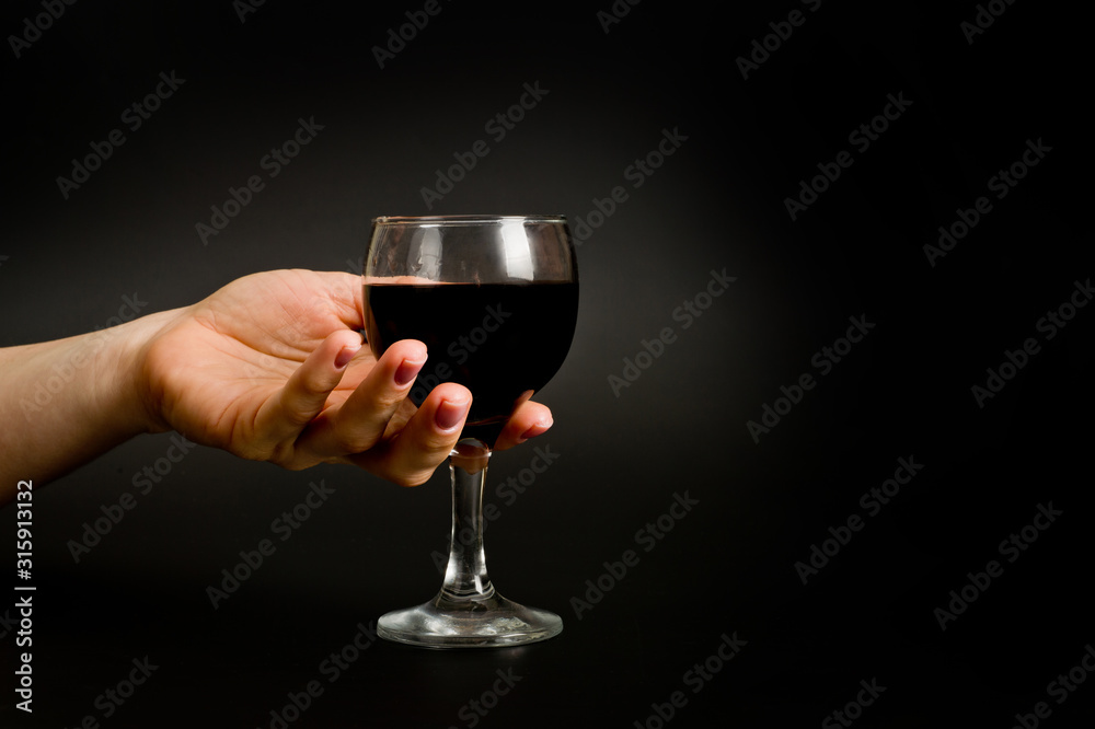 .female hand with a glass of wine on a dark background .female hand with a glass of wine on a dark background