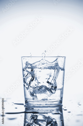 Clear mineral water splashes in a glass with ice. © valkyrielynn