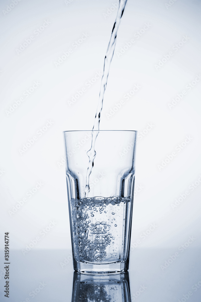 Clear mineral water is poured into a glass with ice. Clear mineral water is poured into a glass with ice.