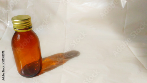 On the left is an empty brown glass bottle of 100 ml from tincture, medicine or pills. Yellow metal lid. To the right is a beige surface for text or elements. 