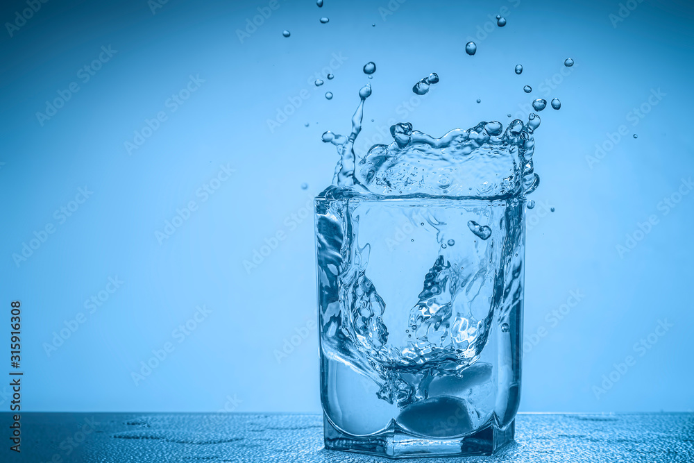 Splash of water in a glass cup on a blue background with place for your text.