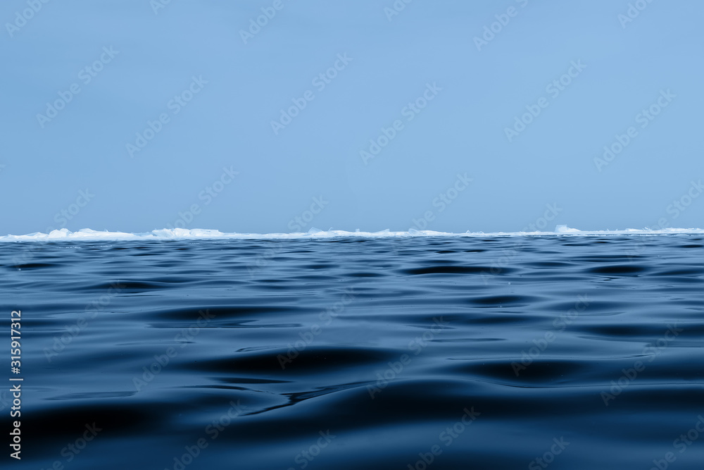 Background texture of blue wavy ice of Lake Baikal with hummocks on the horizon and blue sky