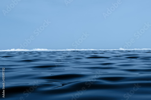 Background texture of blue wavy ice of Lake Baikal with hummocks on the horizon and blue sky