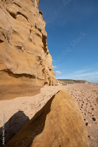 Meeting on Hive Beach in Dorset  England. Beautiful rock formations with large rock in the foreground. Group of people in the background. Blue sky with little cloud.  Beautiful beach in Dorset.