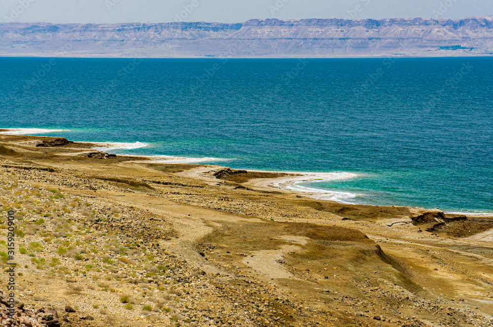 Jordan. Dead Sea. Dead Sea coastline in Jordan. Cliffs descend into emerald water of Dead Sea. Closeup of salt crystals along coast. Waves splash to rocks covered with crystals of salt.