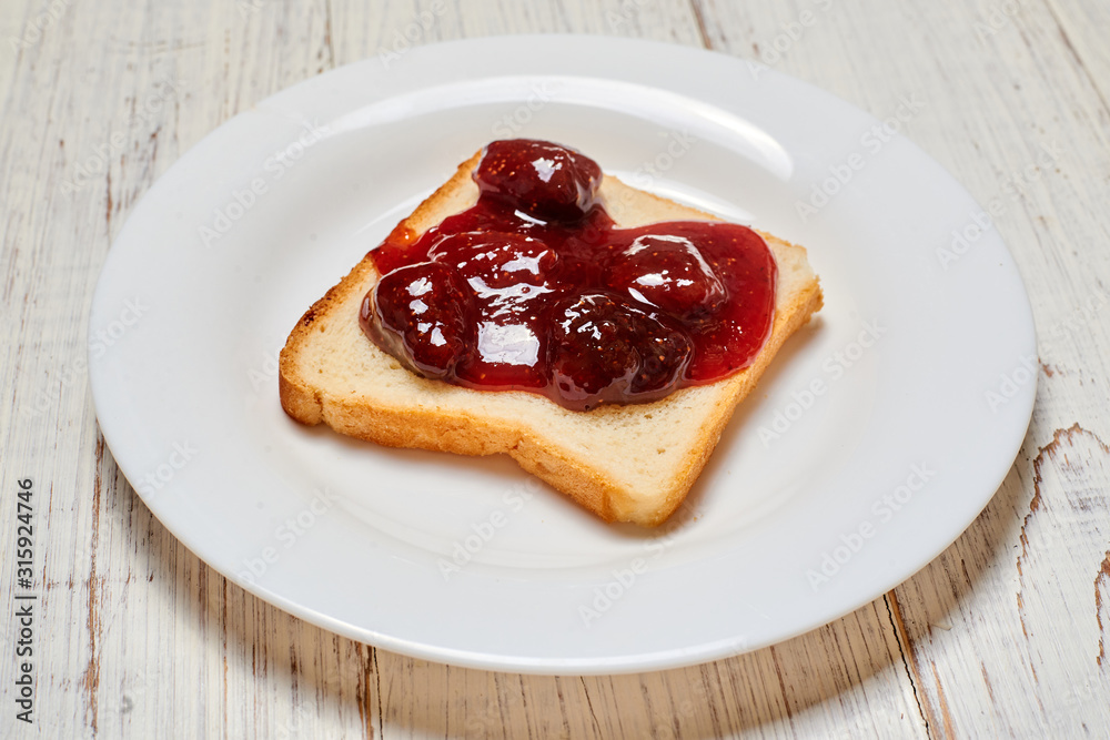 Toast with strawberry jam on a white plate on a light wooden background. Toast with strawberry jam on a white plate on a light wooden background.