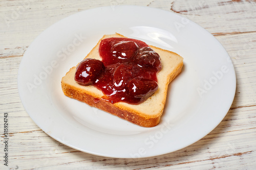 Toast with strawberry jam on a white plate on a light wooden background.