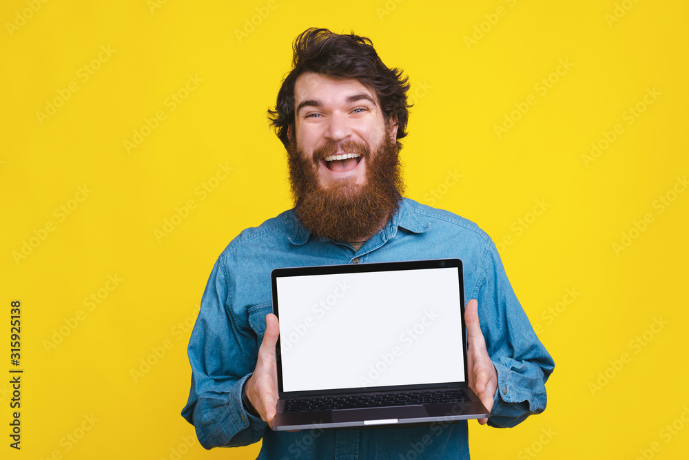 Photo of amazed bearded man showing white screen on laptop