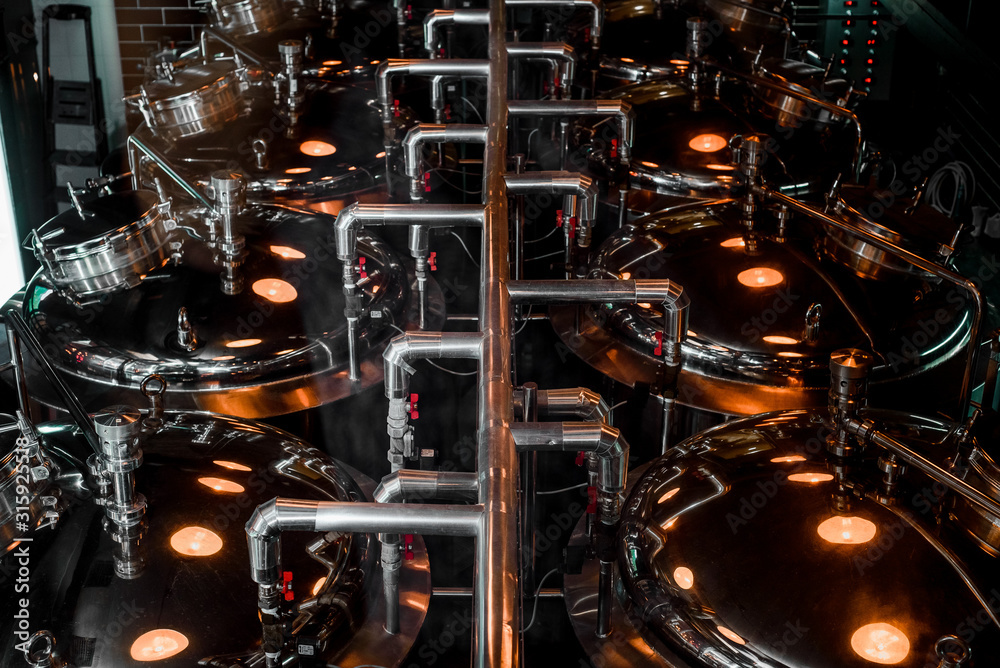 Large reservoirs, tanks and pipes with manometers in private microbrewery. Craft beer production line. Industrial interior background.  View from above.