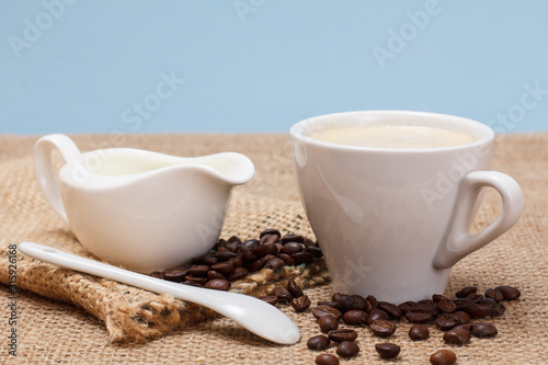 Cup of coffee, cream and coffee beans on sackcloth