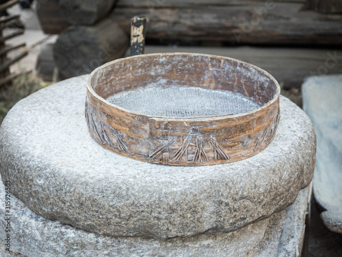 Rotary discoid mill stone for hand-grinding a grain into flour. Medieval hand-driven millstone grinding wheat. The ancient Quern stone hand mill with grain.