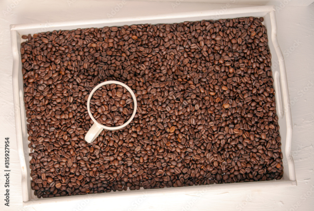 white cup of coffee with coffee grain on grain background. coffee beans top view. Coffee cup and beans view from above. Coffee close-up brown beans texture background. Overflowing beans. white cup of coffee with coffee grain on grain background. coffee beans top view. Coffee cup and beans view from above. Coffee close-up brown beans texture background. Overflowing beans.