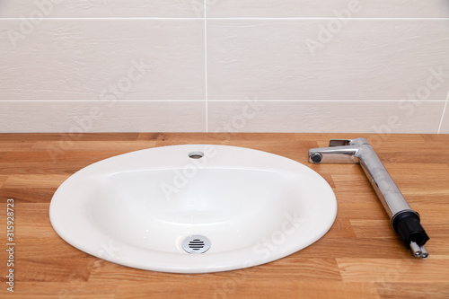 Closeup brown teak wooden empty tabletop with white round ceramic sink and tall silver water faucet. Concept repair, bathroom renovation in apartments, hotel, spa