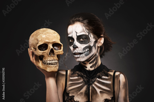 Halloween girl with skull makeup for Halloween on a black background holds a human skull in her hands