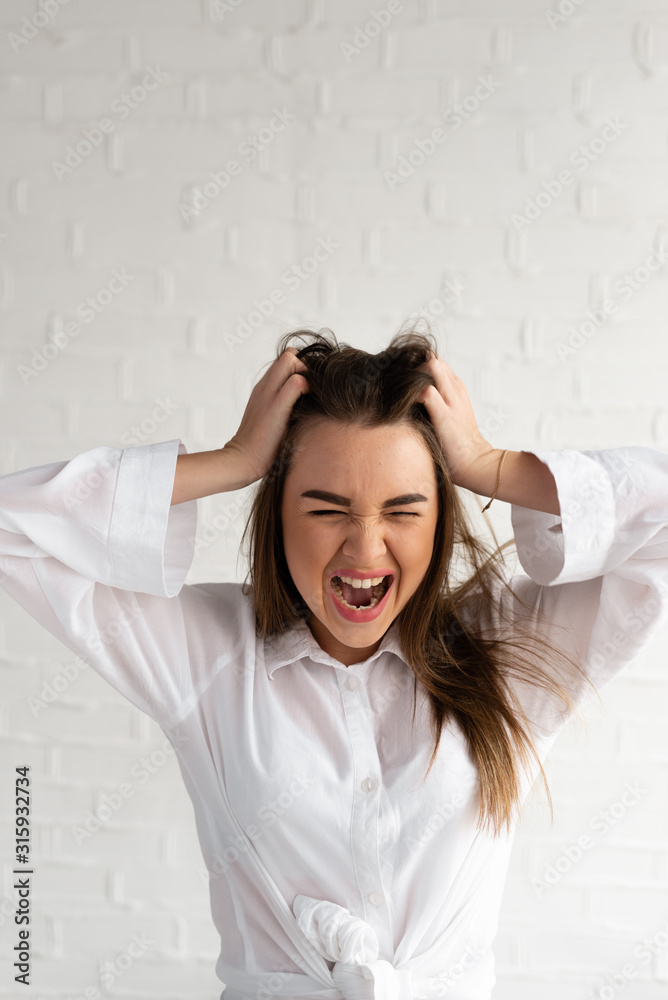 The girl is very angry, holds her hands by her head and shouts, photo on a white background The girl is very angry, holds her hands by her head and shouts, photo on a white background