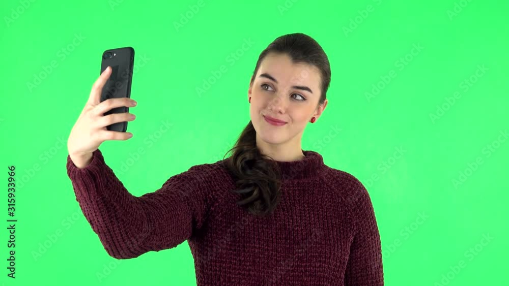 Young woman makes selfie on mobile phone then looking photos on green screen Young woman makes selfie on mobile phone then looking photos on green screen