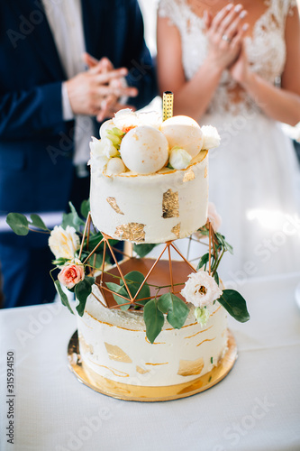 White wedding cake beautifully decorated with flowers,golden flakes and greenery