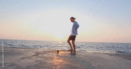 Young handsome male ride on the skateboard , sea and sunset on background