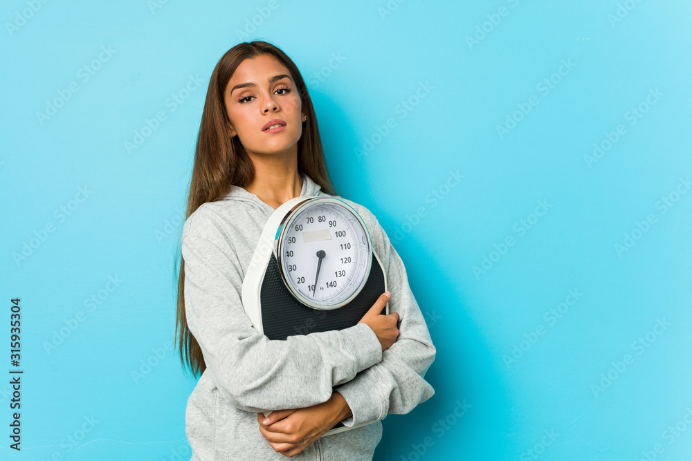 Young caucasian woman holding a scale isolated on a blue background Young caucasian woman holding a scale isolated on a blue background